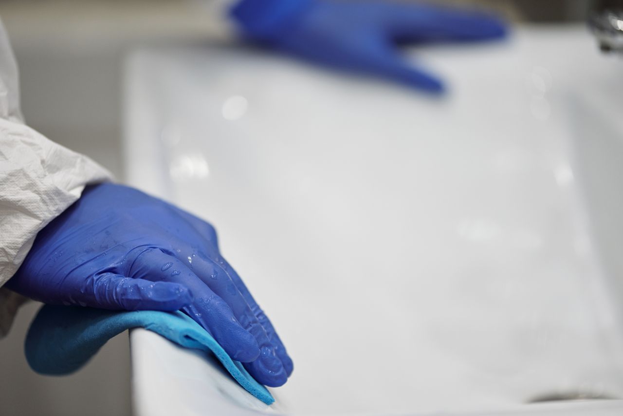 services-03 Gros plan sur une personne nettoyant et désinfectant un lavabo de salle de bain avec des gants et un chiffon, en mettant l’accent sur l’hygiène et la propreté.
